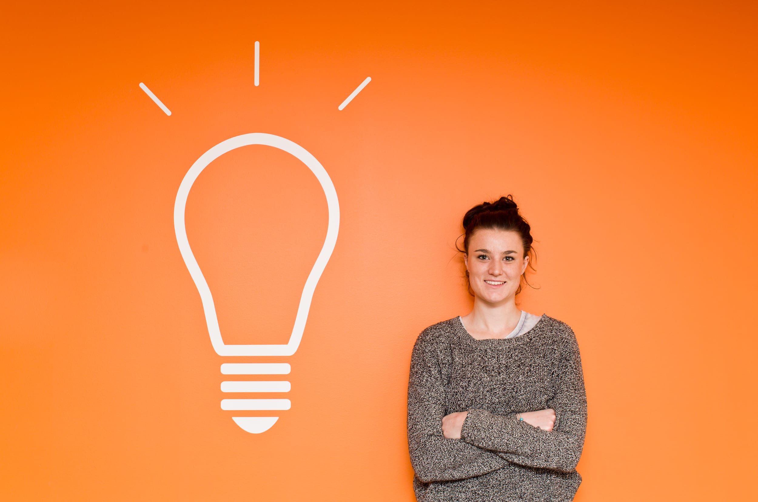 student next to bright orange wall with lightbulb image