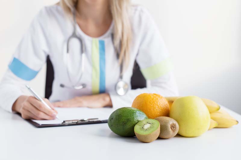 medical professional in background with assortment of fruits in the foreground
