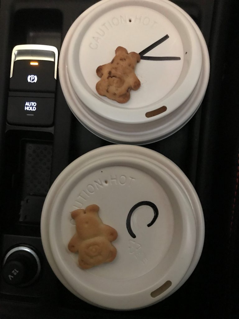 Two cups of coffee with tiny teddies on top of the lids. 