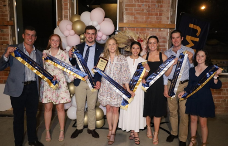 Eight students standing in a line all holding a winner's sash each.
