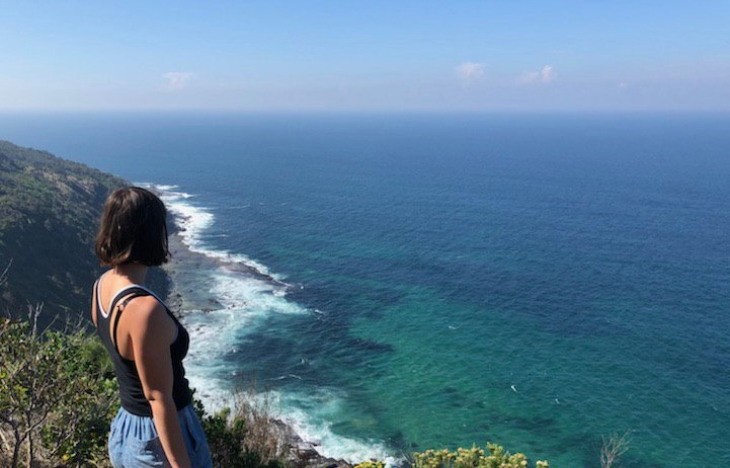 A young woman looking over a cliffside at the ocean.